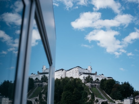 Castle reflected in glass, surrounded by blue sky and clouds.