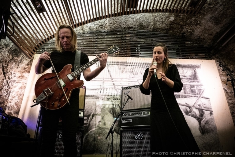 Zwei Musiker performen mit Gitarre und Mikrofon in einem atmosphärischen, gewölbten Raum.